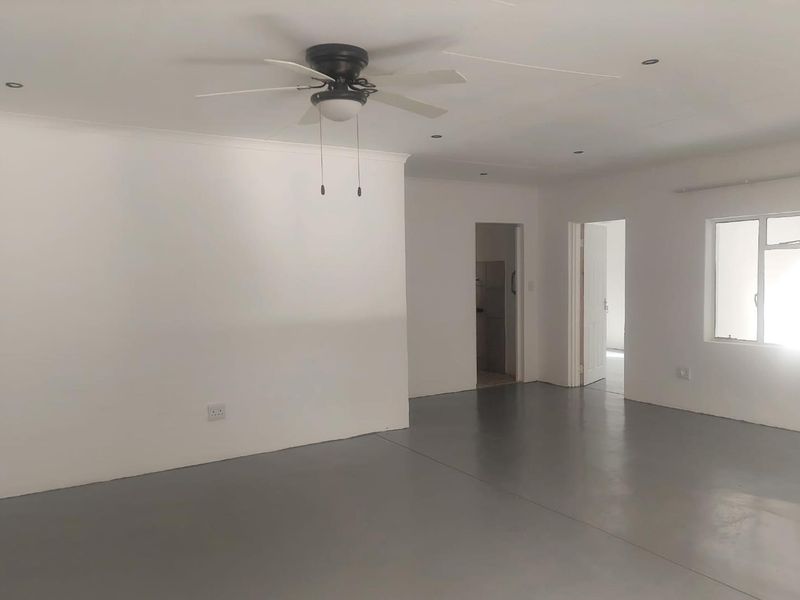 A spacious, empty living area featuring modern epoxy flooring, recessed lighting, and a ceiling fan, offering a clean and neutral blank canvas.