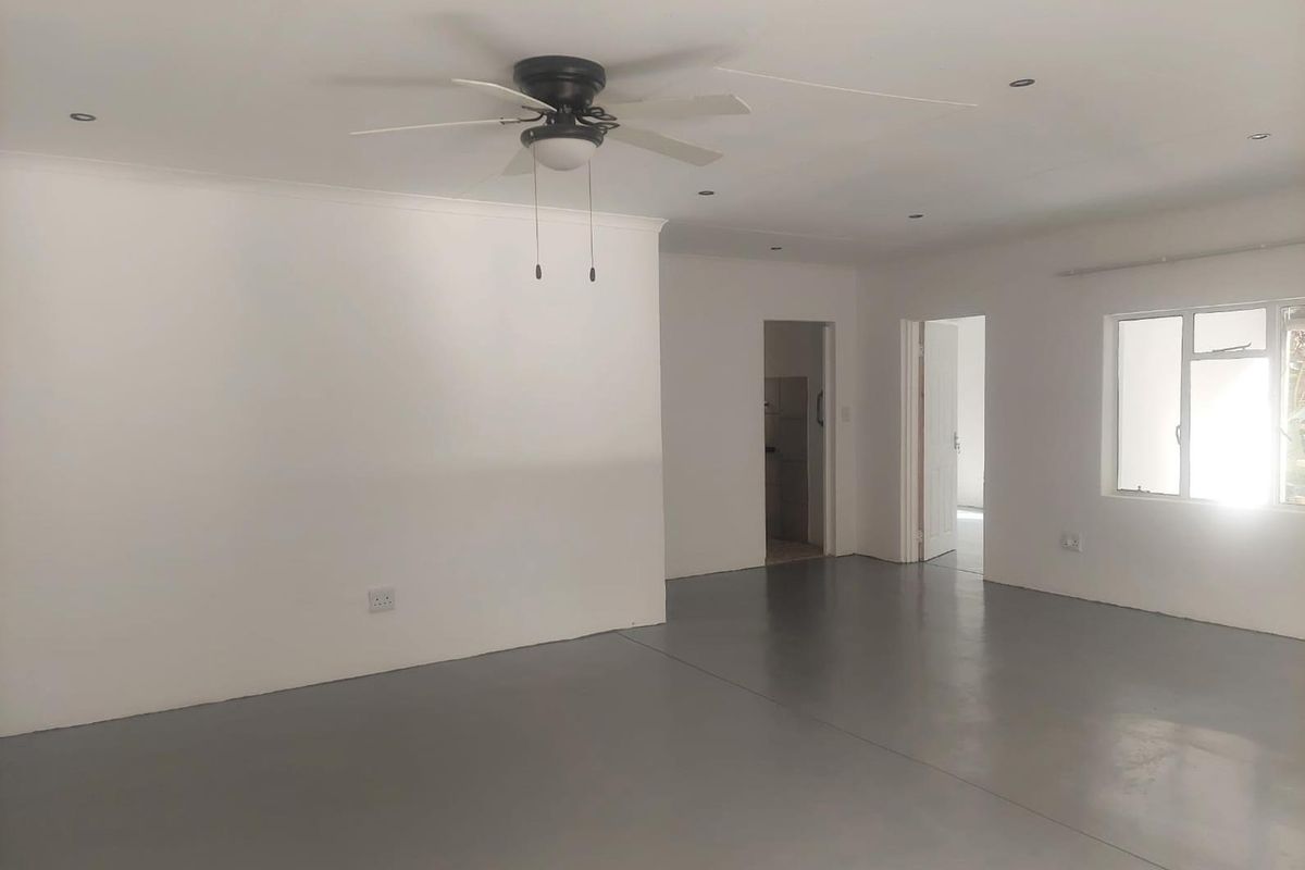 A spacious, empty living area featuring modern epoxy flooring, recessed lighting, and a ceiling fan, offering a clean and neutral blank canvas.