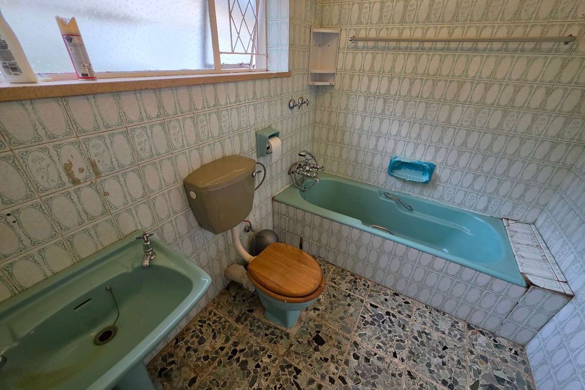 A dated bathroom featuring original pastel green sanitaryware, patterned wall tiles, and terrazzo-style flooring, offering significant potential for a modern renovation.