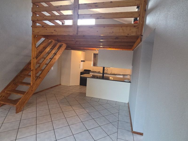 Open plan living area featuring a wooden mezzanine loft with staircase, tiled flooring, and a functional kitchen space.
