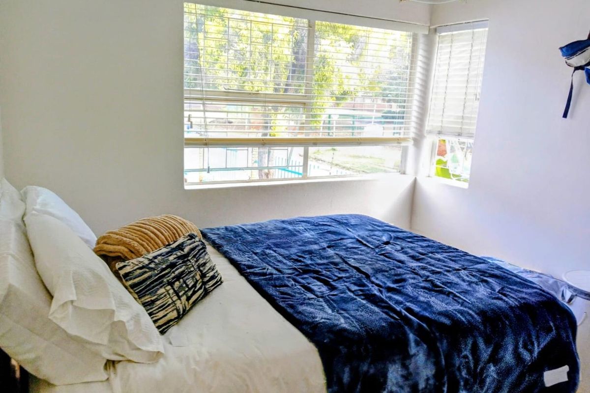 A bright bedroom featuring large windows with fitted venetian blinds, providing natural light and a view of the outdoor area.