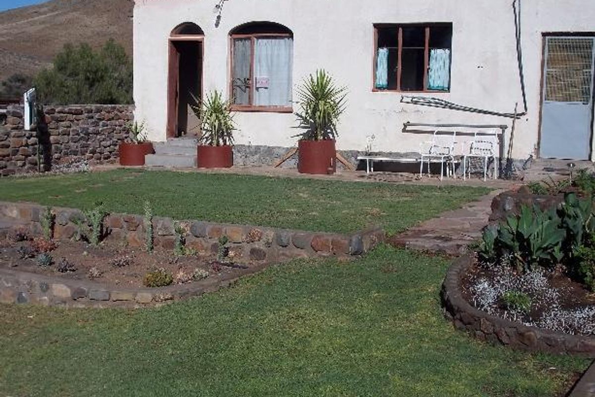 Rear view of a farm dwelling featuring a stone-walled garden, lawn area, and direct access to the building via multiple entry points.