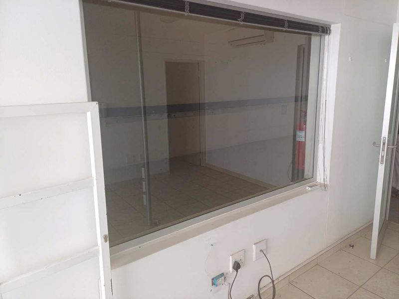An empty office space featuring a large glass partition, tiled flooring, and a wall-mounted air conditioning unit.