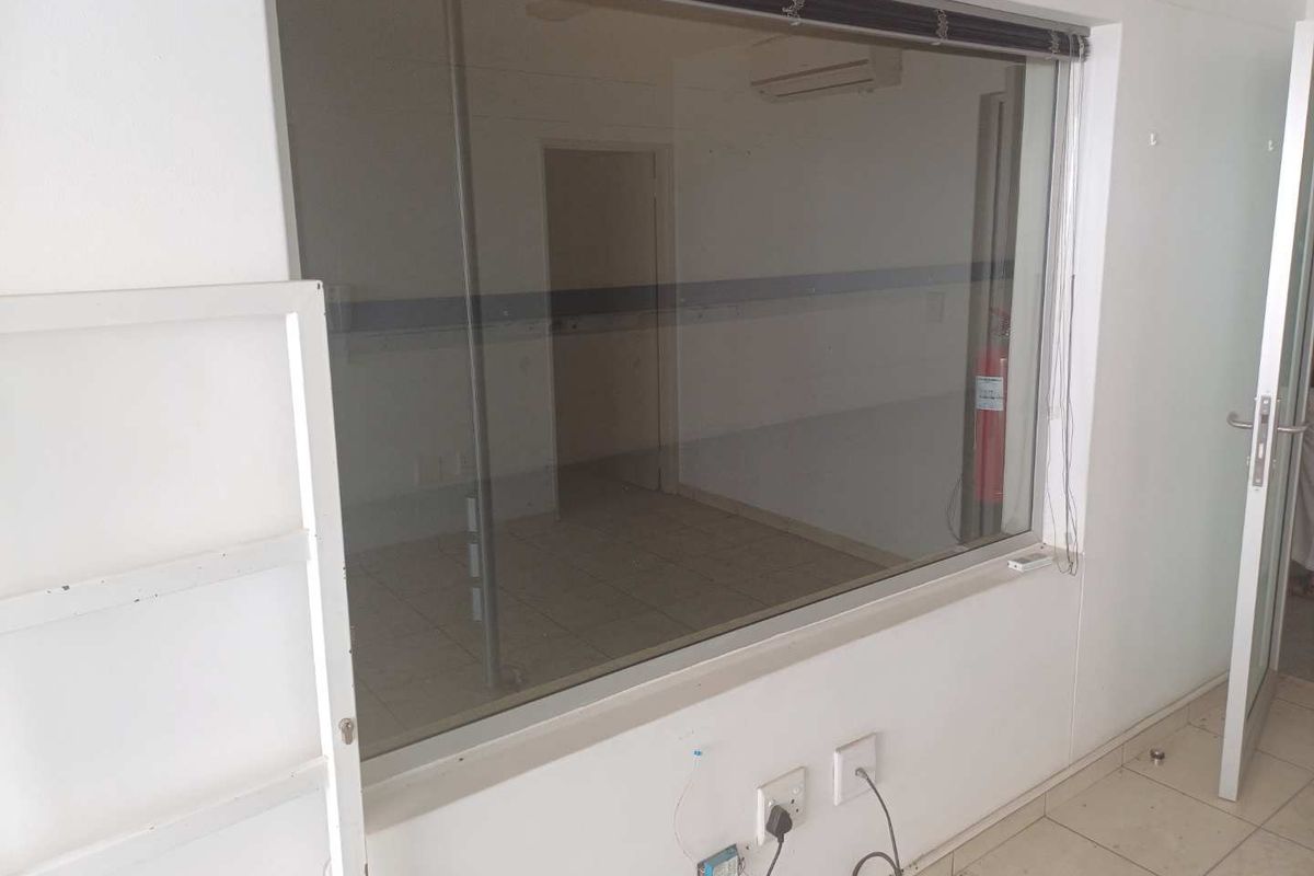 An empty office space featuring a large glass partition, tiled flooring, and a wall-mounted air conditioning unit.