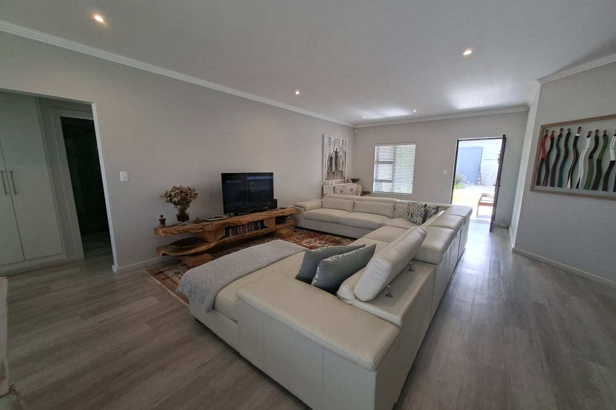 Spacious and well-maintained living room featuring modern laminate flooring, recessed downlighting, and direct access to the outdoor area.