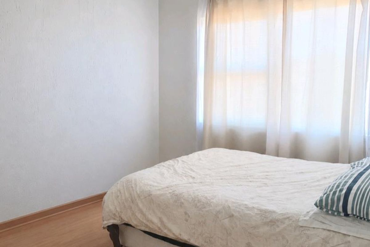 A simple bedroom featuring light-toned laminate flooring, neutral walls, and a coved ceiling, providing a clean and functional living space.