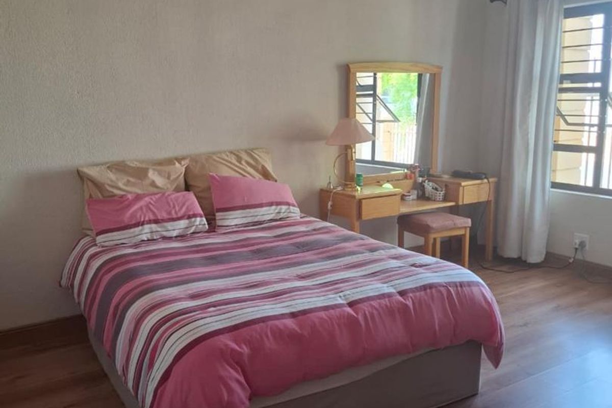 A well-lit bedroom featuring wood-look laminate flooring, neutral wall finishes, and a window with fitted curtain tracks.