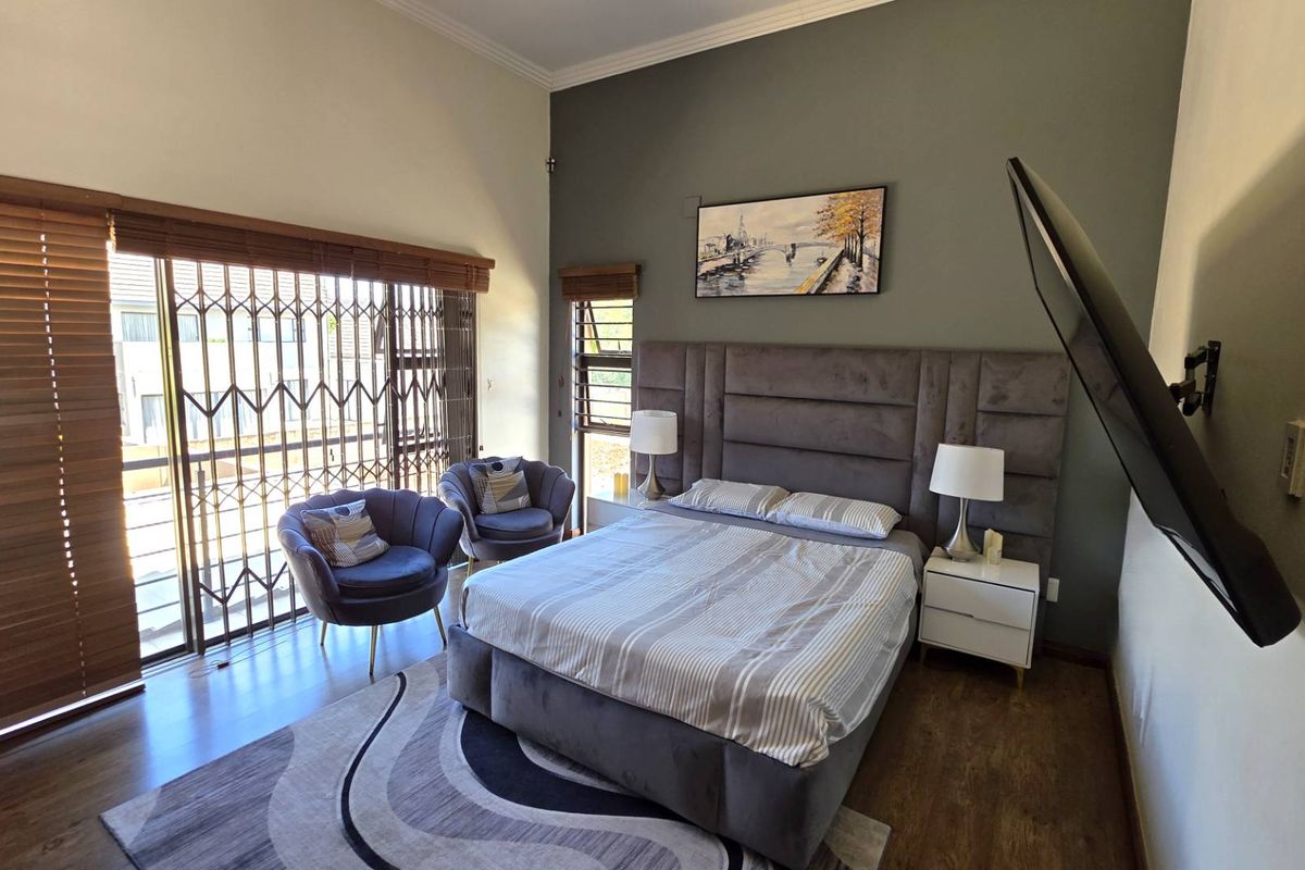 Spacious bedroom featuring high ceilings, large sliding glass doors with security gates, and a feature wall with integrated headboard.