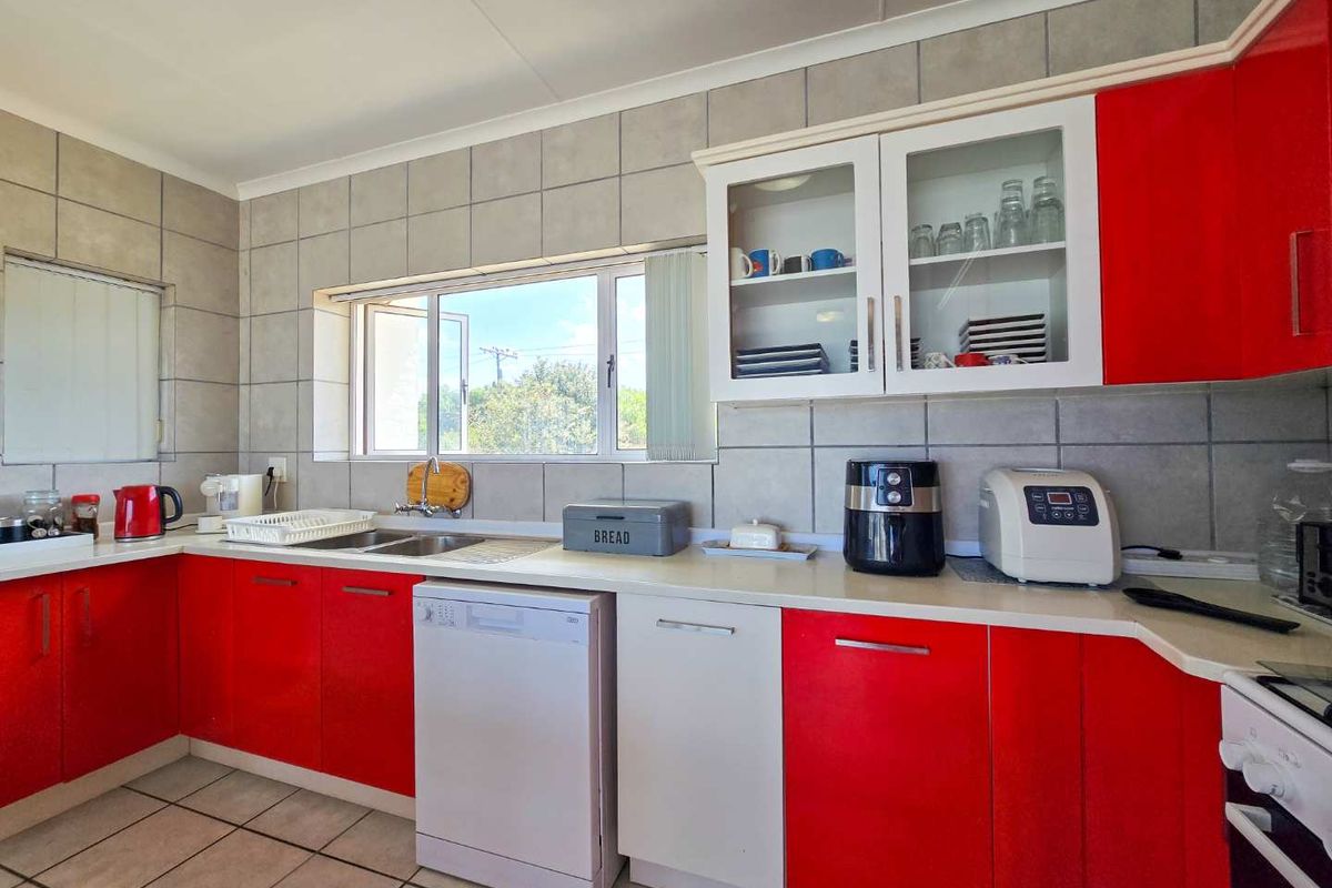 A functional kitchen featuring red and white cabinetry, tiled splashbacks, a double sink, and ample counter space with a window overlooking the exterior.
