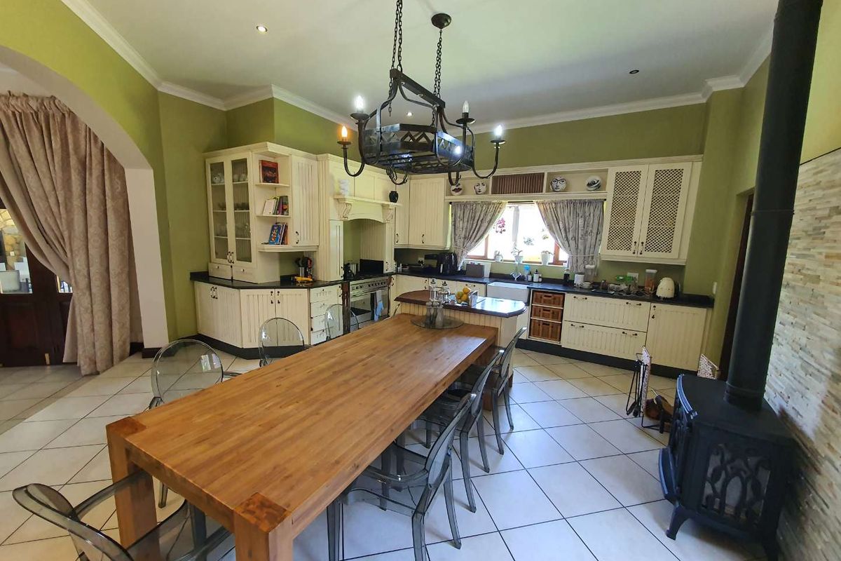 Spacious kitchen featuring cream cabinetry, a central island, farmhouse sink, and a freestanding wood-burning stove, complemented by tiled flooring and decorative lighting.