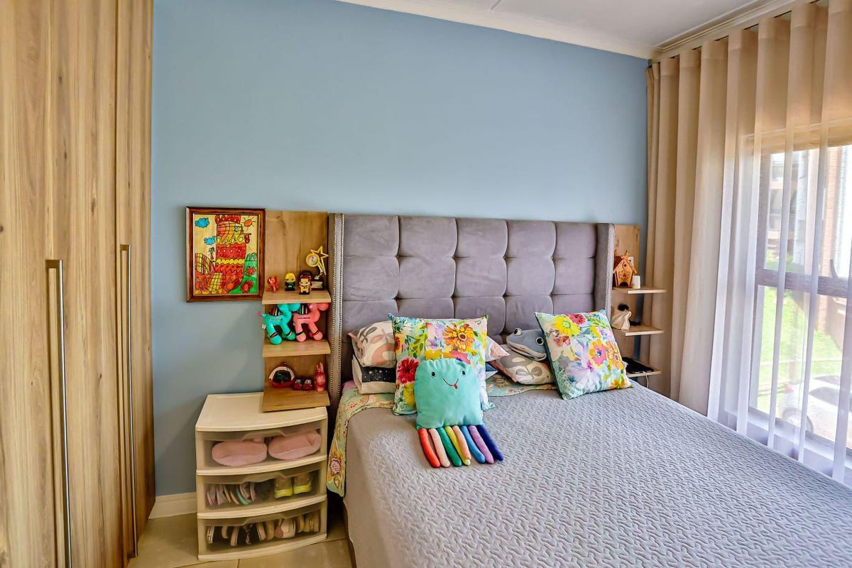 A well-maintained bedroom featuring built-in wooden cupboards, tiled flooring, and large windows with curtain tracks, offering a bright and functional living space.