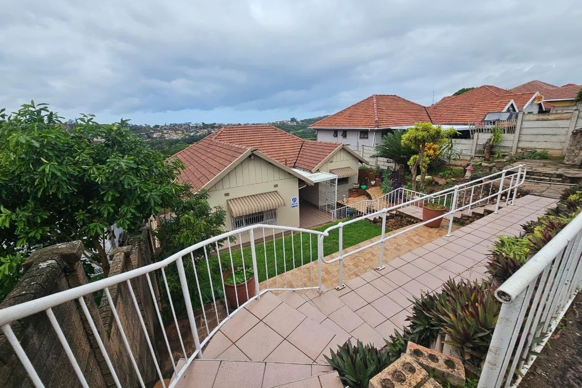 Rear view of the property featuring a tiled staircase with metal handrails, leading down to a garden area with established landscaping and roof views.