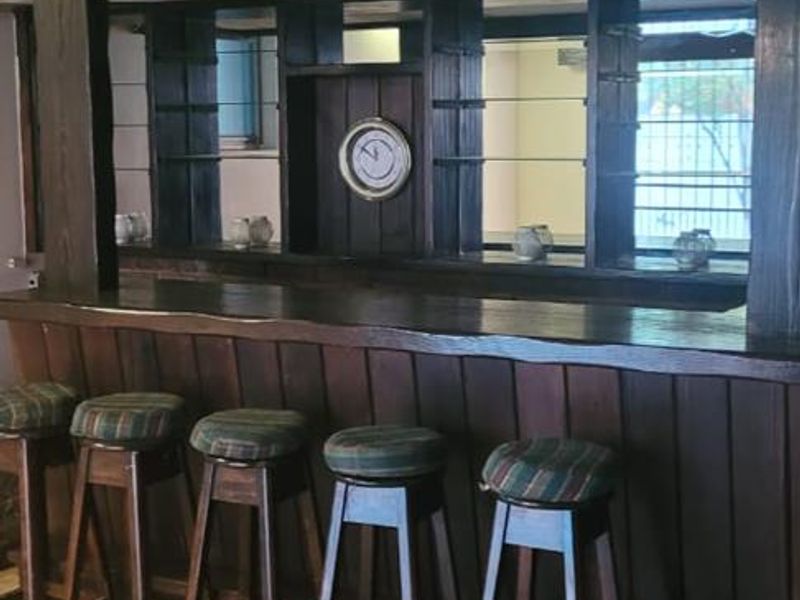 A dedicated home bar area featuring a built-in timber counter, mirrored shelving, and exposed timber ceiling beams, finished with tiled flooring.