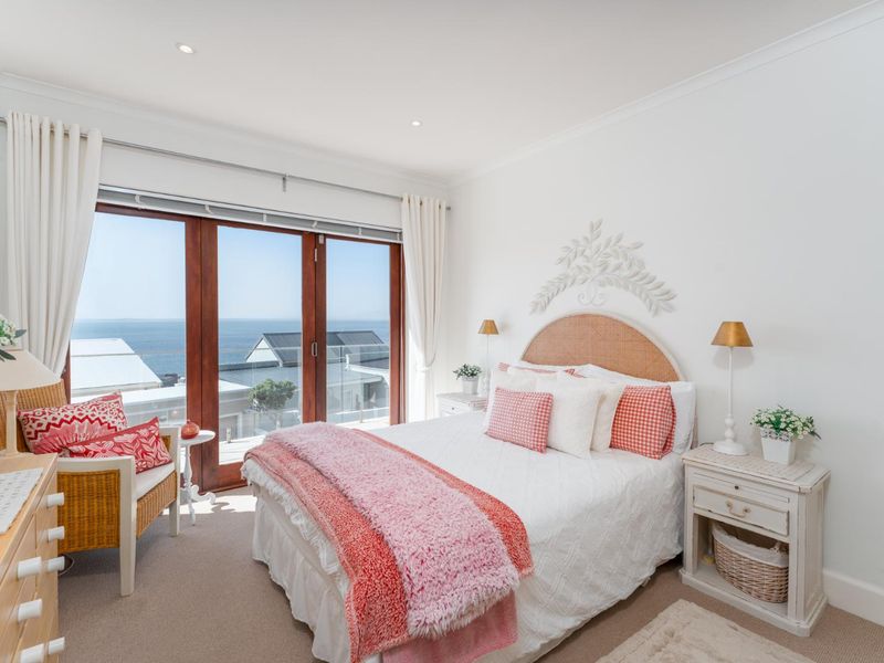 A bright, well-maintained bedroom featuring carpeted flooring, recessed lighting, and large timber-framed sliding doors that open to a scenic ocean view.