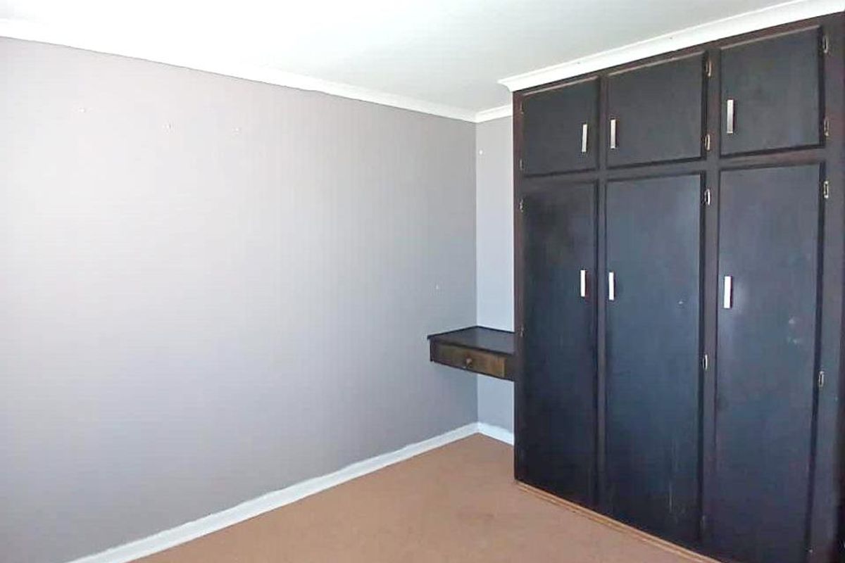 A bedroom featuring built-in dark cabinetry with an integrated desk area, neutral wall tones, and carpeted flooring.