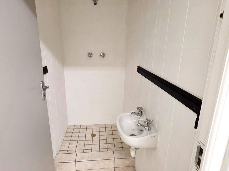 A functional industrial-style bathroom featuring tiled walls and flooring, a wall-mounted basin, and a shower area with a floor drain.