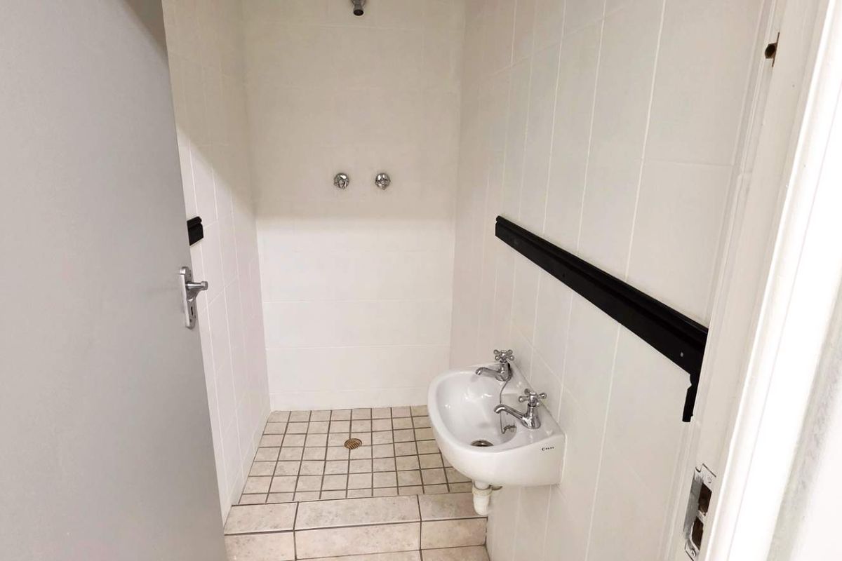 A functional industrial-style bathroom featuring tiled walls and flooring, a wall-mounted basin, and a shower area with a floor drain.
