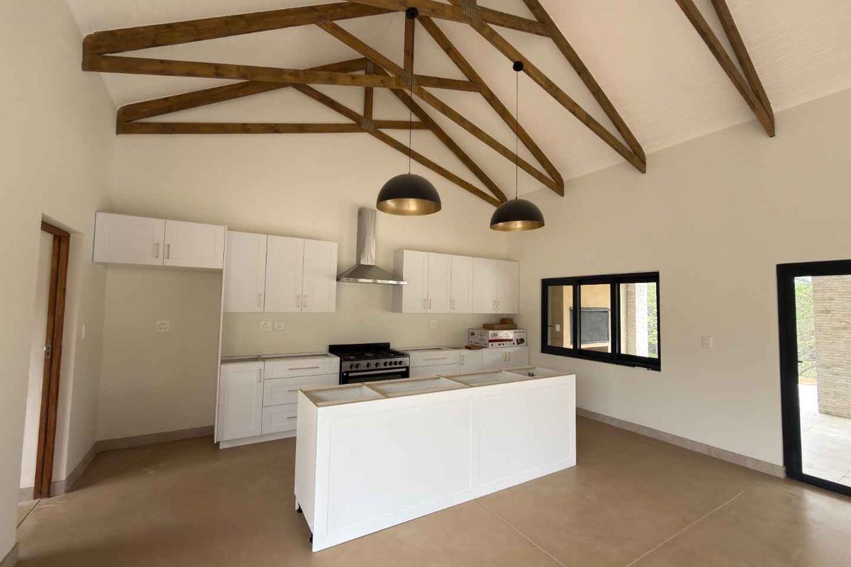 Modern kitchen featuring a large island, white cabinetry, and striking exposed timber trusses under a vaulted ceiling, offering a bright and spacious layout.