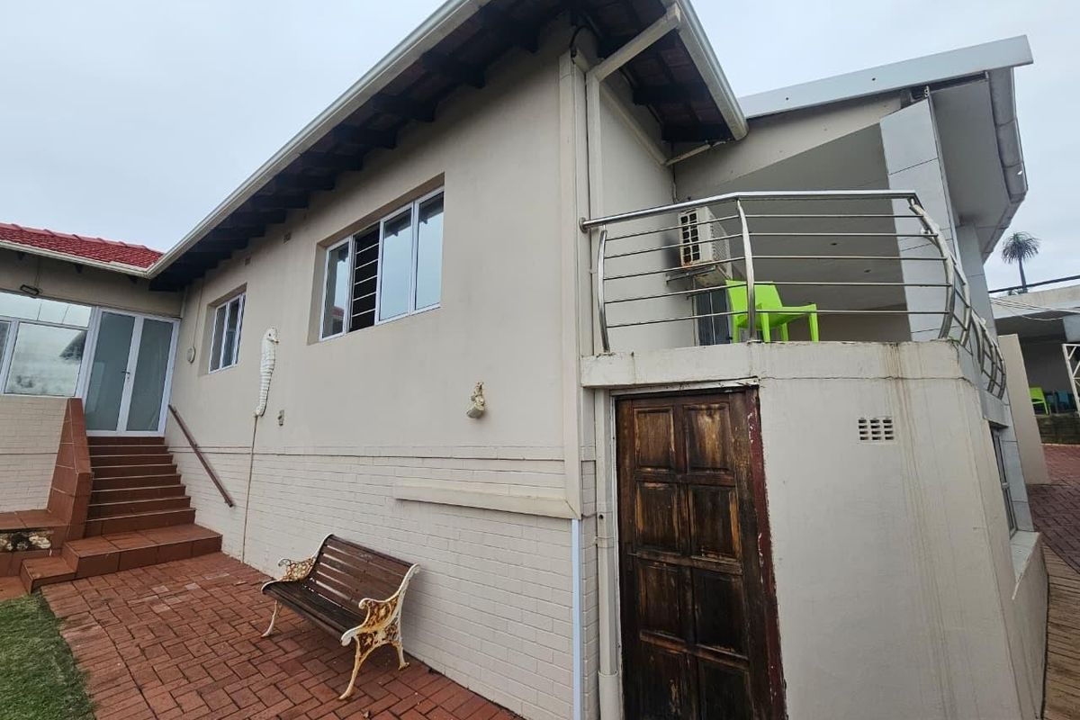 Rear exterior view featuring a paved patio area, staircase access, and an elevated balcony with stainless steel balustrading.
