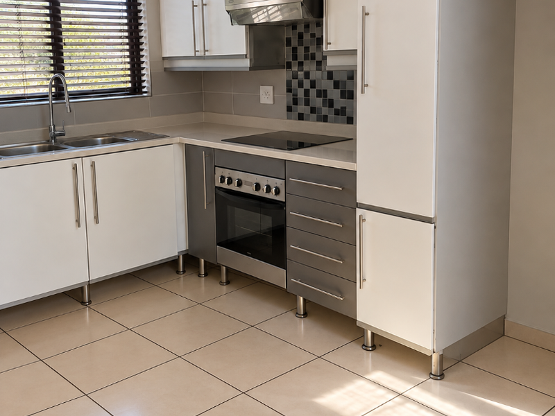 A clean, modern kitchen featuring white and grey cabinetry, integrated appliances including an oven and hob, tiled flooring, and a functional sink area.