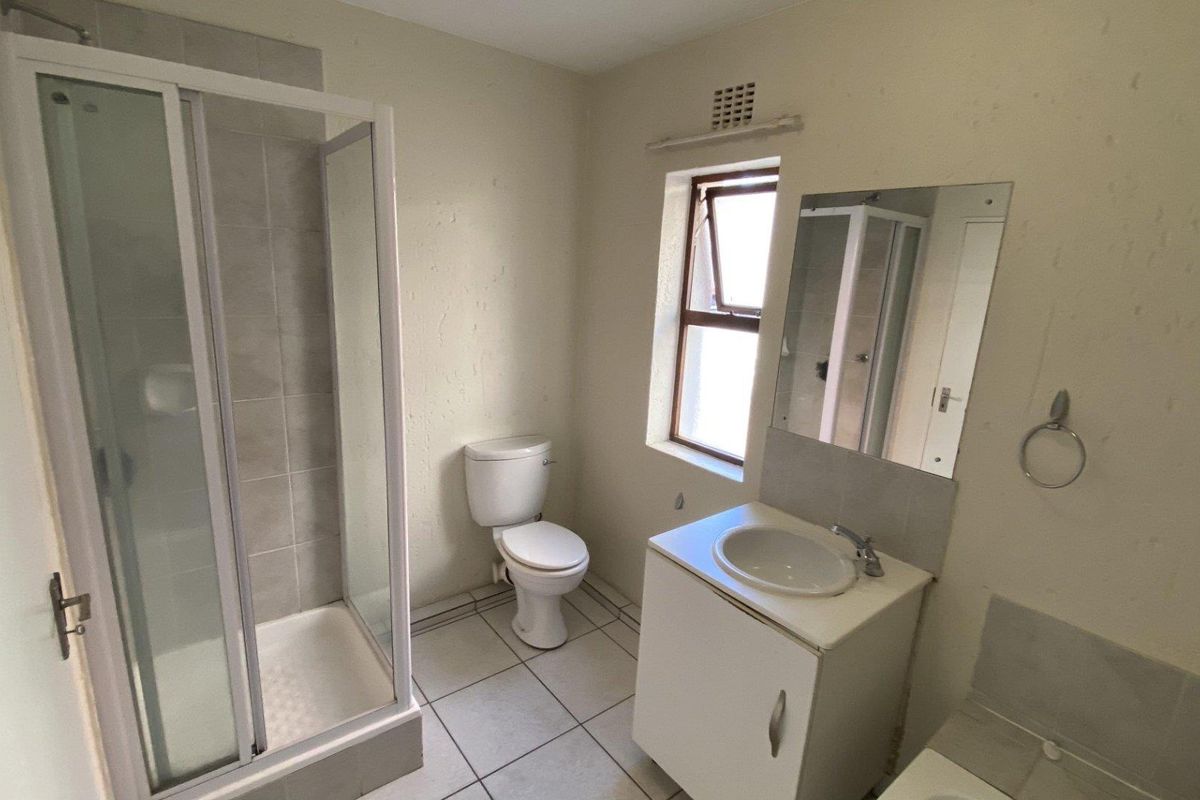 A functional bathroom featuring a shower enclosure, a vanity unit with a basin, and a toilet, with tiled flooring and neutral wall finishes.
