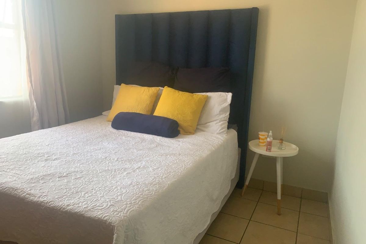 A bedroom featuring tiled flooring and a large blue upholstered headboard, providing a simple and functional sleeping space.