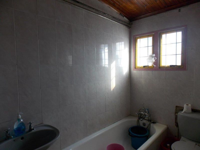 A dated bathroom featuring a bathtub, basin, and toilet with tiled walls and a timber ceiling, requiring modernization.