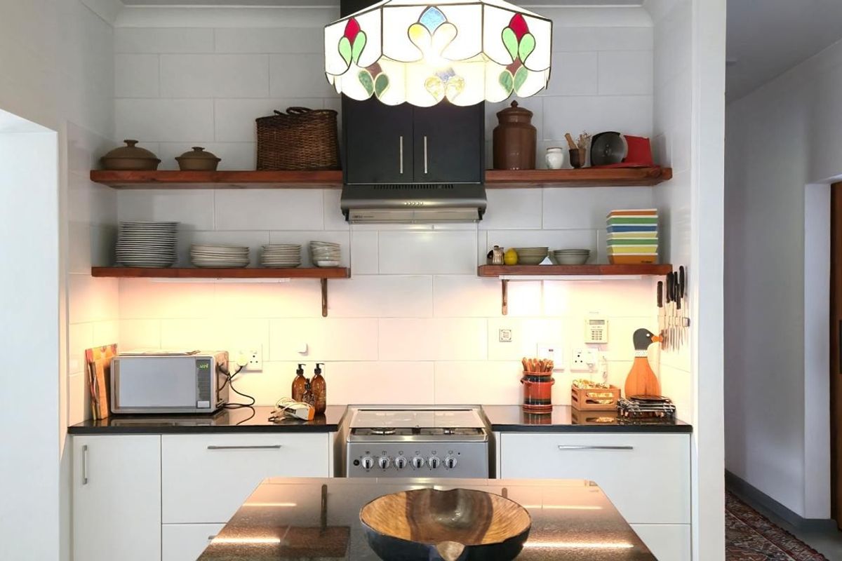 A modern kitchen featuring white cabinetry, dark stone countertops, open timber shelving, a stainless steel stove, and a built-in extractor fan.