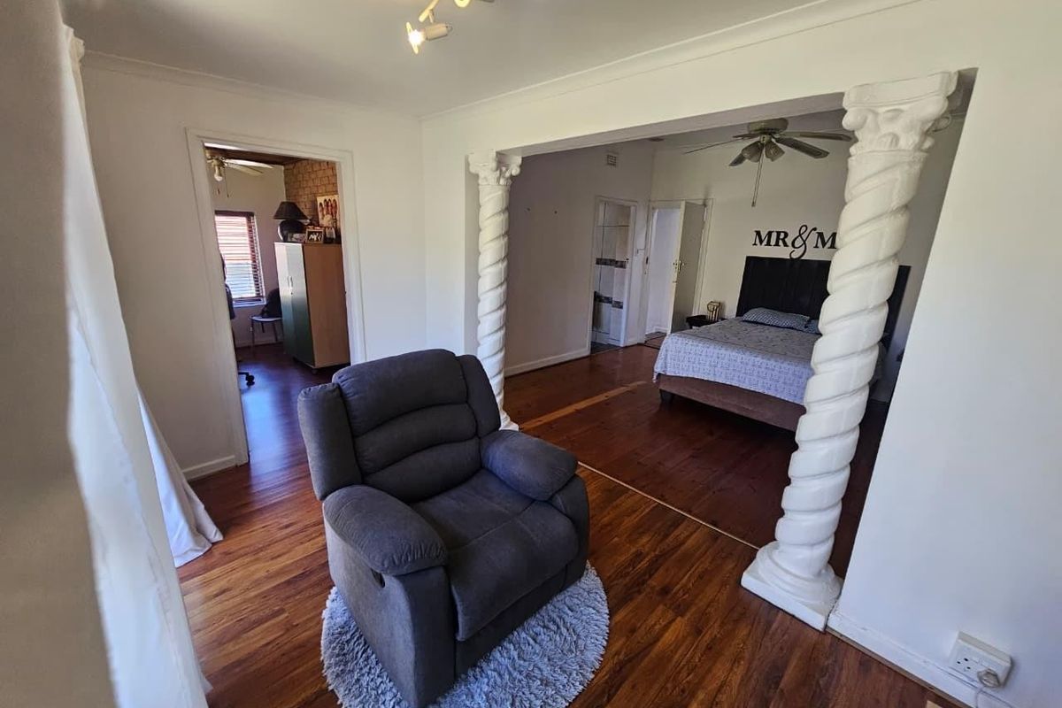 Spacious bedroom featuring hardwood flooring, decorative columns, and a ceiling fan, offering a unique layout with an adjoining space.