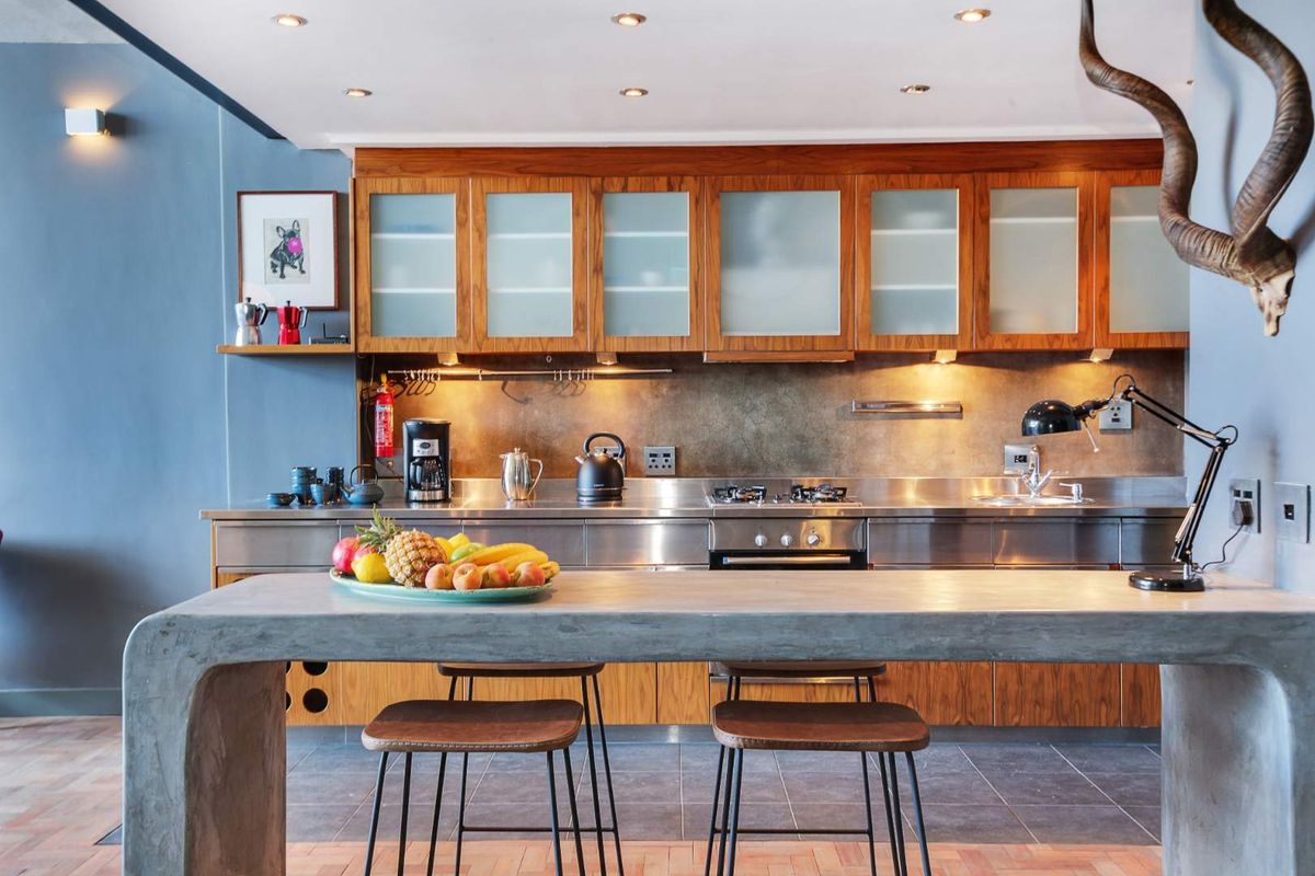 Modern kitchen featuring wooden cabinetry, stainless steel countertops, integrated appliances, and a concrete breakfast bar with recessed lighting.