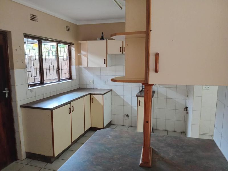 An empty kitchen featuring dated built-in cabinetry, laminate countertops, tiled splashbacks, and security bars on the windows.