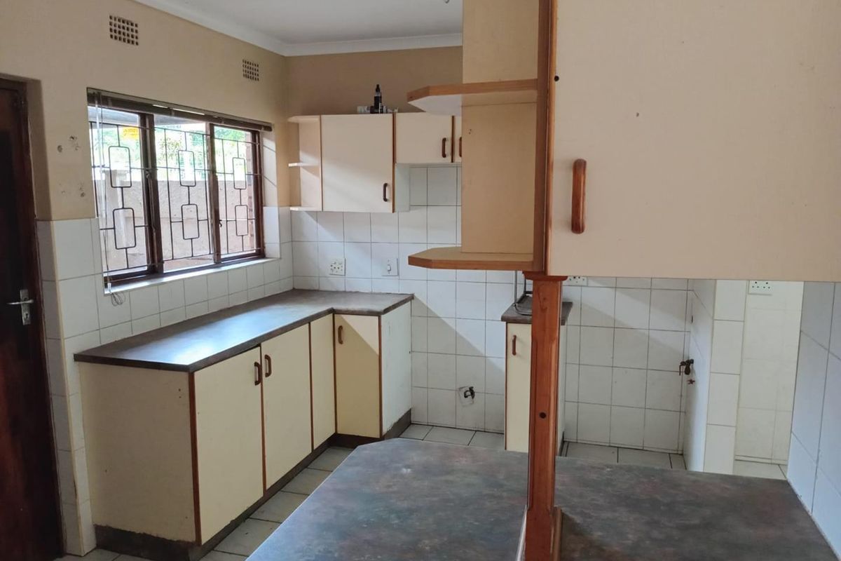 An empty kitchen featuring dated built-in cabinetry, laminate countertops, tiled splashbacks, and security bars on the windows.