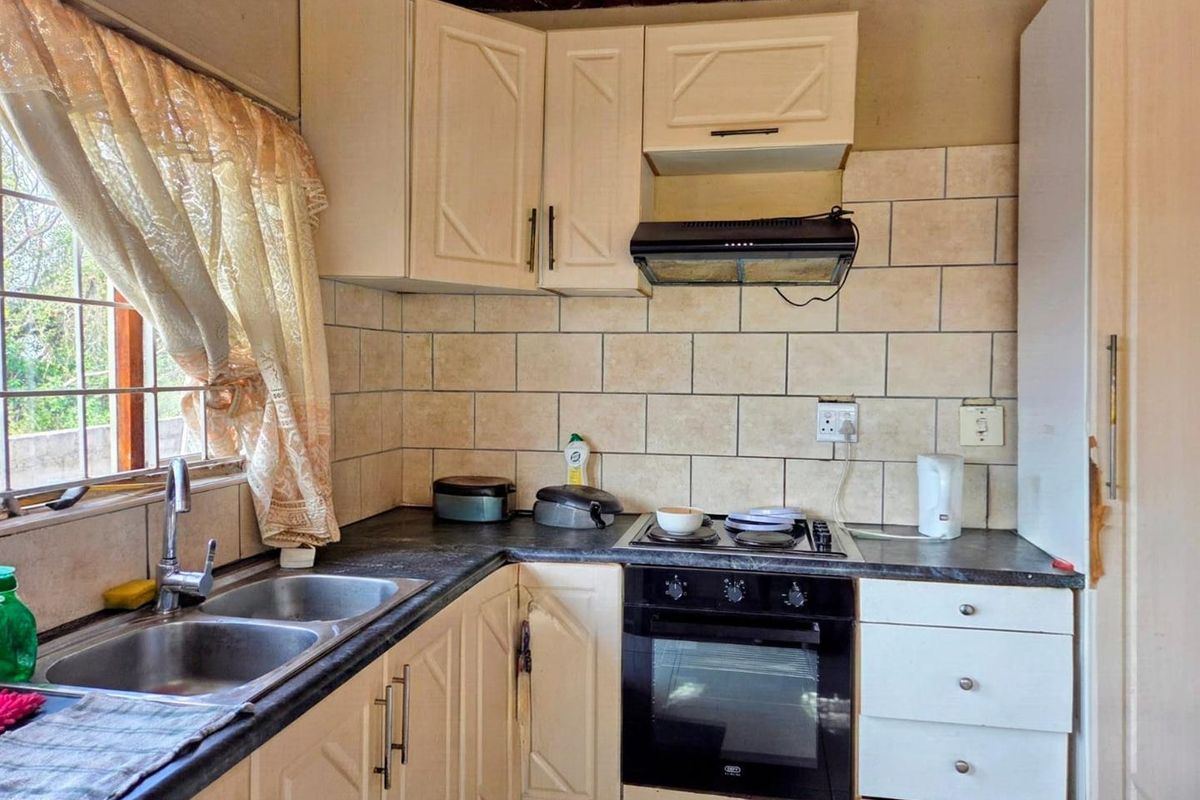 Compact kitchen featuring built-in cabinetry, a double basin sink, and integrated oven with hob, requiring cosmetic updates to modernize the space.