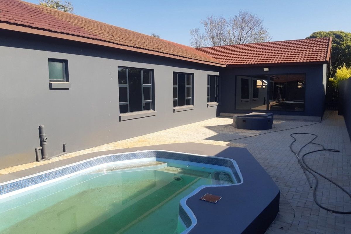 Rear exterior view featuring a paved patio area, a built-in fire pit, and a swimming pool set against the dark grey rendered house facade.