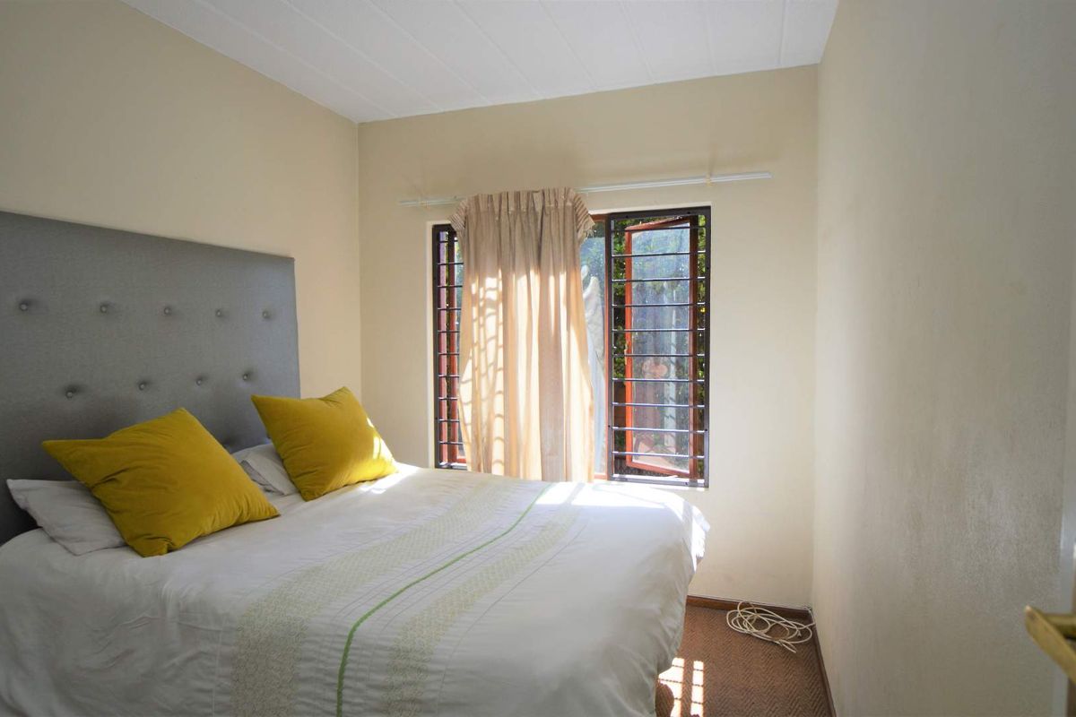A functional bedroom featuring carpet flooring and a window fitted with security bars, providing natural light and ventilation.
