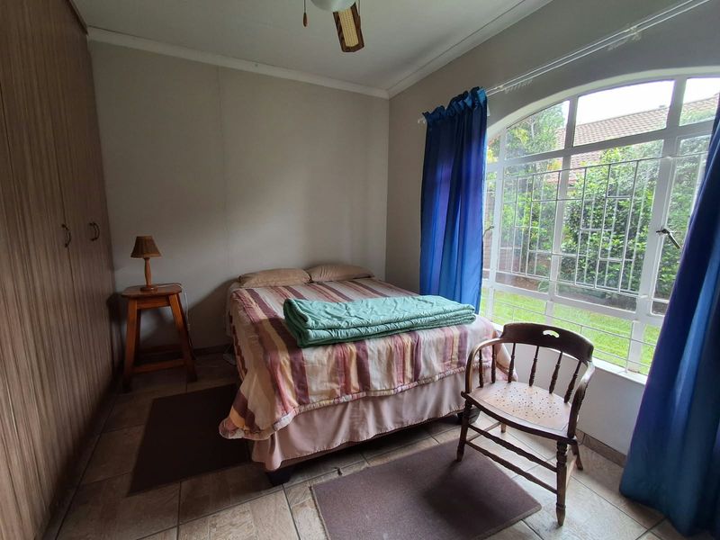 A bedroom featuring built-in cupboards, tiled flooring, and an arched window with security bars overlooking the garden.