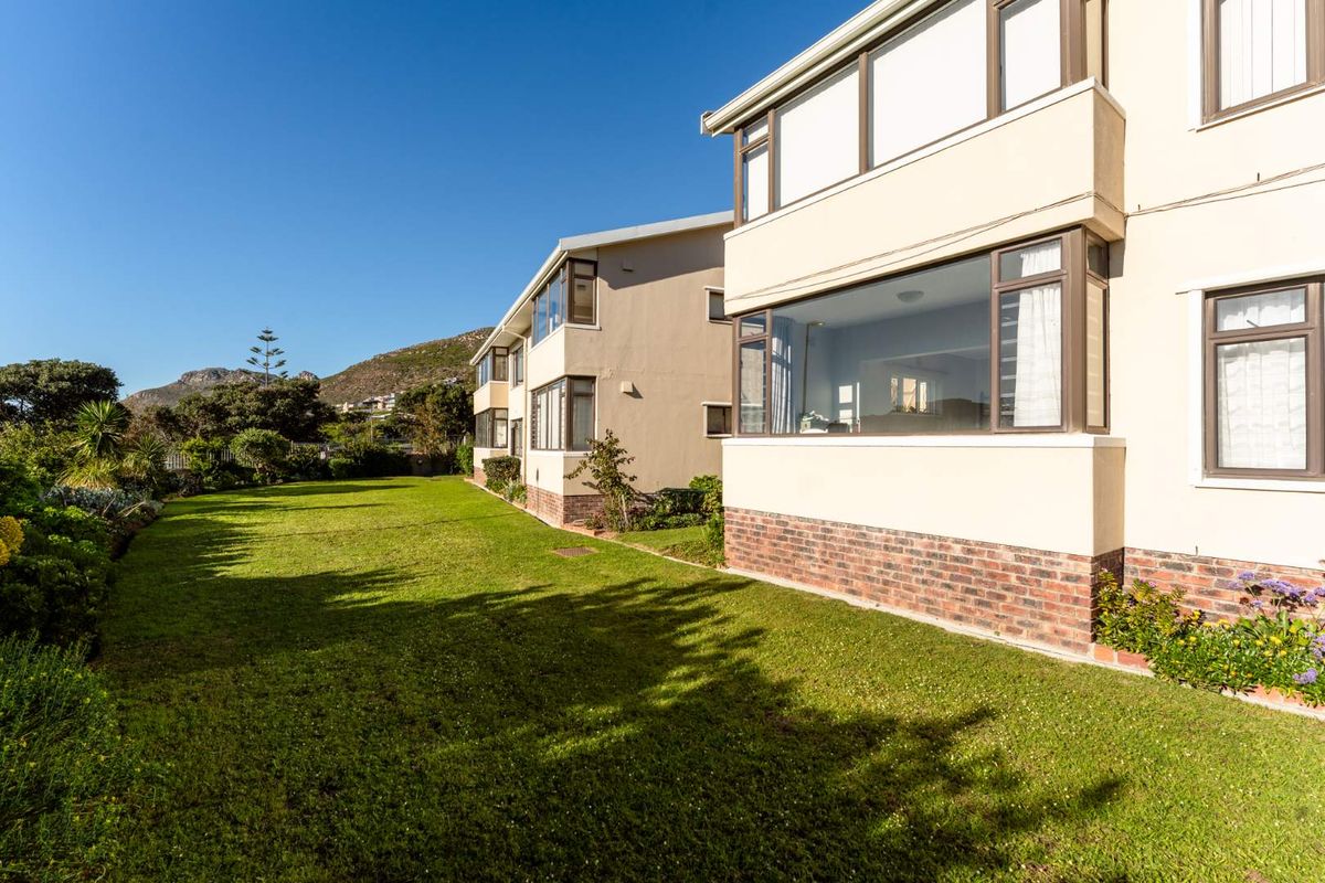 Rear view of the apartment building featuring a well-maintained lawn, brick base detailing, and large windows overlooking the garden area.