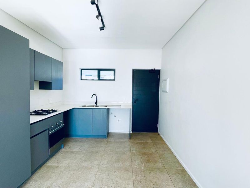 Modern kitchen featuring dark grey cabinetry, gas hob, built-in oven, double sink, and neutral tiled flooring in an open-plan layout.