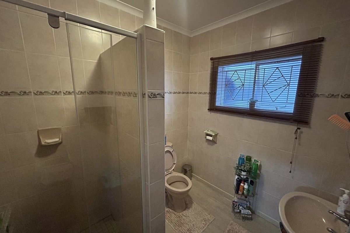 A functional bathroom featuring a glass-enclosed shower, a standard toilet, and a wall-mounted basin with neutral wall tiles.