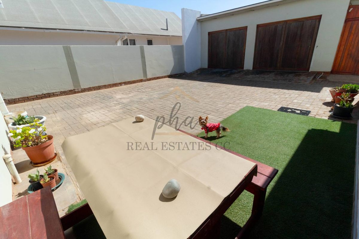 A paved rear courtyard area featuring a double garage with wooden doors and a section of artificial lawn.
