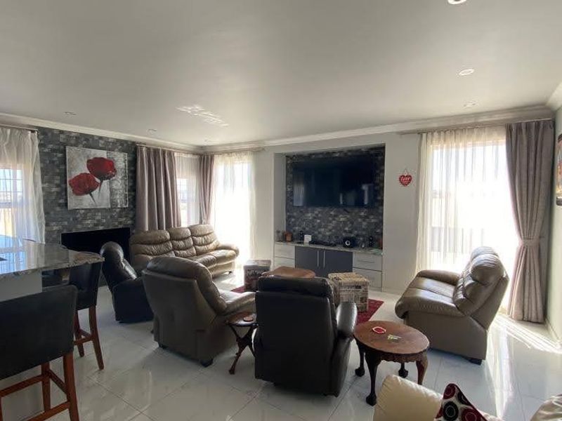 Spacious open-plan living area featuring a modern stone-clad feature wall, built-in media cabinetry, recessed lighting, and sleek porcelain floor tiles throughout.