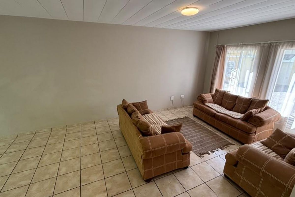 A spacious living room featuring neutral wall tones, tiled flooring, and large windows with security bars, offering a bright and functional living space.
