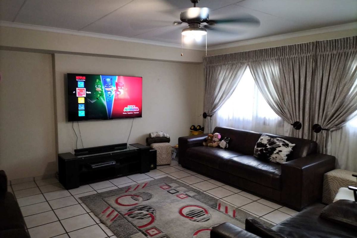 A comfortable living room featuring tiled flooring, a ceiling fan, and large window treatments, providing a functional space for relaxation.