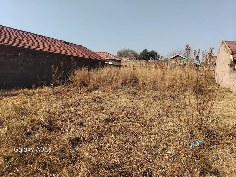 A vacant residential plot featuring overgrown dry grass and perimeter boundary walls, offering a blank canvas for future development.