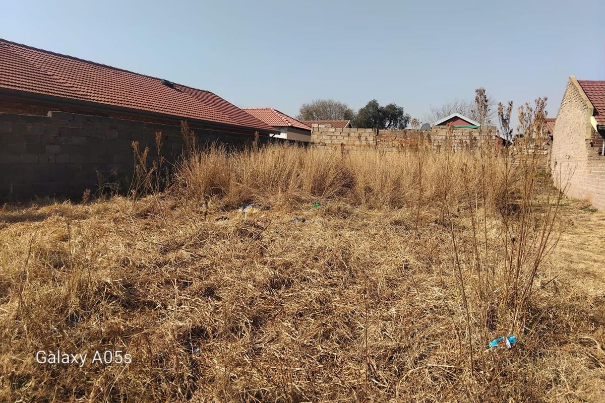 A vacant residential plot featuring overgrown dry grass and perimeter boundary walls, offering a blank canvas for future development.