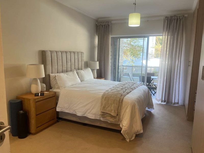 A well-maintained bedroom featuring built-in cupboards, neutral carpeting, and a sliding glass door providing access to a private balcony.