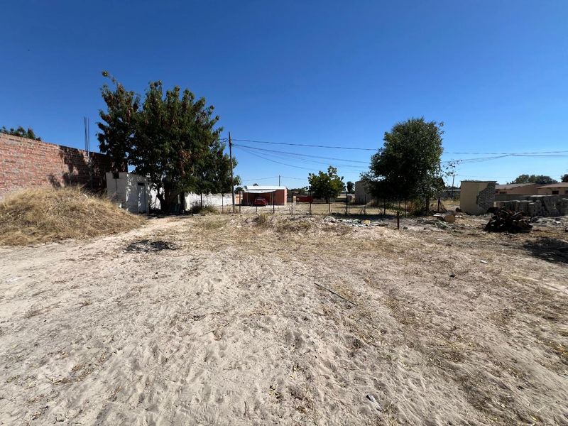A large, undeveloped rear plot featuring sandy ground, perimeter brick walling, wire fencing, and a small outbuilding structure.