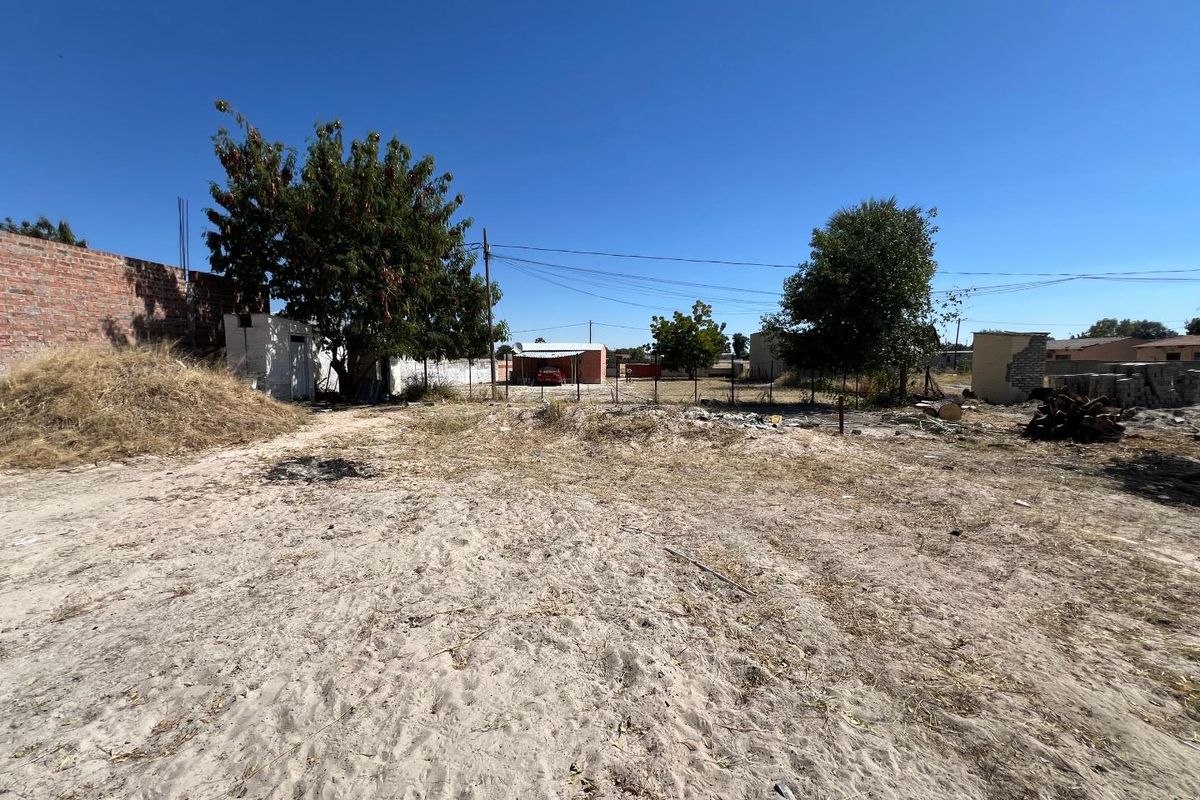 A large, undeveloped rear plot featuring sandy ground, perimeter brick walling, wire fencing, and a small outbuilding structure.