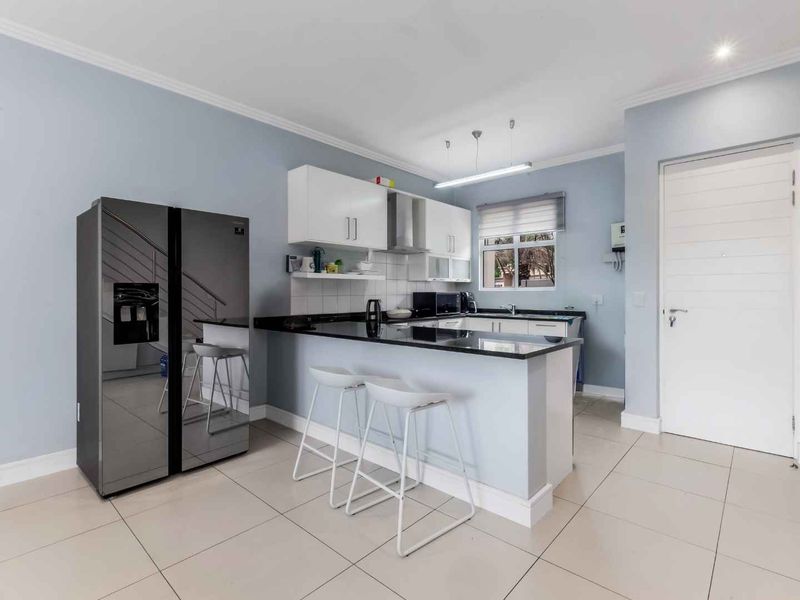 Modern kitchen featuring sleek granite countertops, ample built-in cabinetry, a stainless steel extractor fan, and neutral tiled flooring in an open-plan layout.