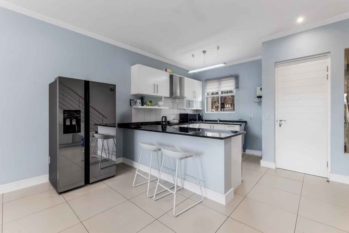 Modern kitchen featuring sleek granite countertops, ample built-in cabinetry, a stainless steel extractor fan, and neutral tiled flooring in an open-plan layout.
